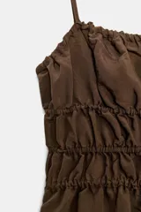 Vestido midi color marrón oscuro, con escote recto fruncido y tirantes finos ajustables. La falda es de corte amplio y cae con caída.