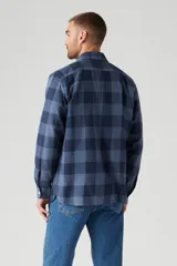 Camisa de manga larga azul a cuadros, con cuello clásico, cierre frontal con botones, dos bolsillos con solapa abotonada en el pecho y corte recto.