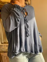 Blusa color marrón claro confeccionada en lino, de manga larga con elástico en los puños, escote en V con doble lazo y corte irregular.