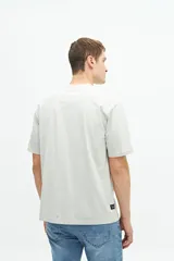 Remera gris claro de manga corta con cuello redondo y estampado azul con texto circular en el pecho.