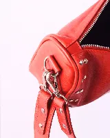 Bandolera marrón de cuero con tachas plateadas y correa de cuero con tachas plateadas. Tiene dos asas desmontables, una corta con tachas para llevarla en la mano o al hombro y una larga para llevarla al hombro o cruzada.