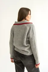 Cárdigan gris de tejido con relieve, cuello camisero, botones al frente y detalles de color rojo en cuello y puños.