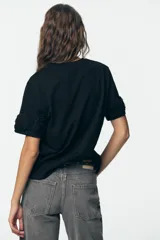 Camiseta negra de algodón con cuello redondo, manga corta y detalle de flores con volumen en las mangas.