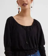 Blusa de poliéster negra con mangas largas abullonadas, escote redondo con botones y bordado en el frente. Tiene volados en el ruedo y ajuste con lazos en los laterales.