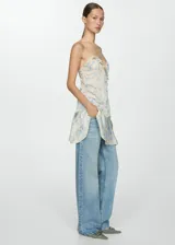 Vestido corto color crema con estampado floral en tonos azules y verdes, con escote en V, breteles finos y volados en el escote y ruedo. Presenta lentejuelas bordadas y cierre lateral invisible.