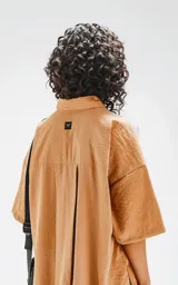 Camisa manga corta color beige, con cuello clásico, cierre frontal con botones, doble bolsillo con ojal en el delantero y silueta oversize.