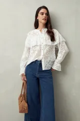 Camisa negra semitransparente de encaje bordado con diseño geométrico. Tiene silueta fluida, mangas largas y volados en el frente y los hombros.