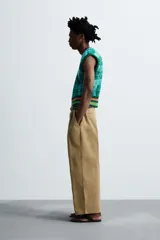 Pantalón color beige de corte ancho, con pliegues frontales dobles, bolsillos laterales y traseros de vivo. Largo cropped y cierre frontal con cremallera y botón.