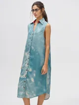 Vestido camisero largo celeste con efecto tie-dye, cuello camisero con solapas rojas, sin mangas y abotonado al frente.