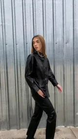 Camisa negra de cuero ovino italiano, con mangas largas, hombros caídos y calce oversize. Tiene cierre frontal con broches metálicos.