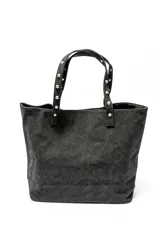 Bolso tipo shopper color negro con apliques de tachas plateadas en los bordes y las asas.