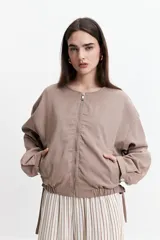 Campera corta color verde militar, sin cuello, con cierre frontal y elástico en la cintura. Tiene bolsillos amplios y mangas largas con puños elásticos.