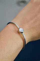 Pulsera rígida plateada de alpaca con detalle de nácar circular.