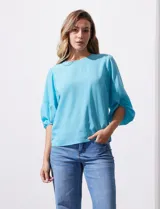 Blusa celeste de gasa marca Sioni, con mangas cortas amplias con abertura y botón.