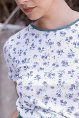 Remera blanca con estampado floral en tonos violeta y verde, cuello redondo con ribete verde y corte ajustado.