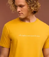Remera de hombre color mostaza, de corte comfort, con cuello redondo y manga corta. Estampa frontal con la frase "La confiance est le secret du succès" en color blanco.