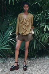 Camisa color verde oliva de tela traslúcida con escote en V, mangas largas abullonadas con puños elásticos y volantes en el frente.