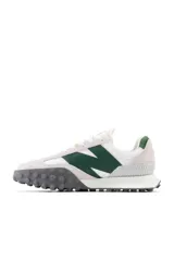 Championes New Balance de estilo casual, con capellada en gamuza color gris claro, logo "N" en verde oscuro y suela de goma con diseño texturizado en gris oscuro.