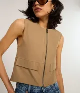 Chaleco color beige de corte sastrero con cierre frontal de cremallera, cuello redondo y bolsillos con solapa.