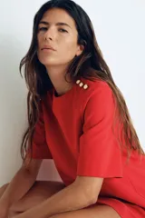 Vestido corto rojo con cuello redondo y manga corta. Presenta detalle de botones dorados en el hombro.