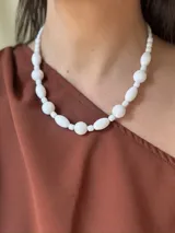 Collar corto de cuentas blancas de diferentes formas y tamaños, unidas por un hilo transparente.