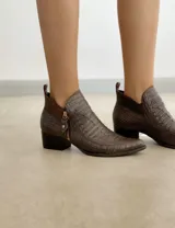 Botín de cuero color marrón claro, con punta fina, cierre lateral con cremallera dorada, detalle de pespuntes en el empeine y taco cuadrado de madera color negro.