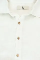 Camisa de manga larga color blanco hueso, confeccionada en lino, con cuello clásico y cierre frontal con botones de coco.