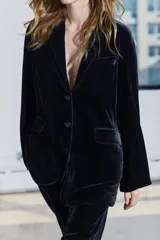 Blazer de terciopelo negro con cuello solapa de muescas, manga larga con abertura y botones, bolsillos con solapa y forro interior.