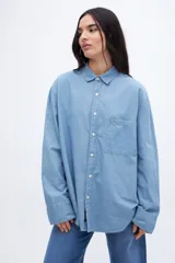 Camisa celeste de denim de algodón, con cuello solapa clásico, bolsillo cuadrado en el pecho, botones personalizados y calce oversize.