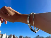 Pulsera rígida doble de acero quirúrgico plateado, con forma curva y recta.