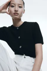 Cárdigan negro de punto con cuello redondo, manga corta y cierre frontal con botones dorados.