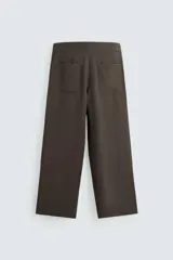 Pantalón marrón de corte ancho, con cintura ajustable con cordón, bolsillos delanteros y traseros tipo parche, detalle de costuras verticales en el frente y cierre frontal con cremallera y gancho metálico oculto.