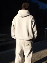 Conjunto deportivo gris compuesto por un hoodie con bolsillo canguro y un pantalón de jogging con bolsillos laterales y trasero. Ambos con logo de la marca en negro.