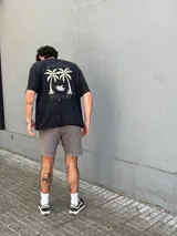 Remera negra de corte oversize con estampa en la espalda de dos palmeras y un ángel en una hamaca.