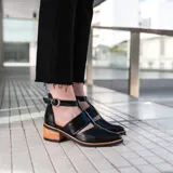 Zapato de cuero negro con detalle de charol, taco de madera con folia en cuero de 5cm, cierre YKK en talón, hebilla y elástico en el empeine.