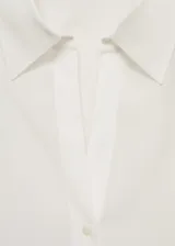 Camisa blanca de tejido fluido, con cuello camisero, cierre frontal con botones, mangas largas y puños abotonados.