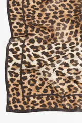 Pañuelo cuadrado con estampado de leopardo en tonos marrones y beige, con borde liso color marrón oscuro.