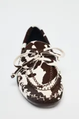 Zapato tipo mocasín en piel con pelo, con estampado animal, detalle de lazo en la parte delantera, pespunte en contraste y acabado en punta redonda.