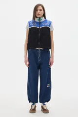 Chaleco de fleece color crema con cuello alto, cierre frontal con cremallera y bordados de rombos en color borgoña. El chaleco es reversible y tiene elástico en la cintura para ceñir a gusto.