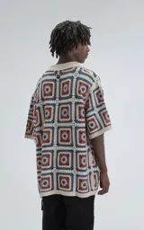 Camisa de manga corta tejida a crochet en punto abierto, con cuello tipo polo y cierre frontal con botones. Diseño con cuadrados de colores beige, naranja y azul. Corte oversize.