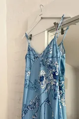 Vestido midi celeste con estampado floral en tonos azules y blancos, de breteles finos y corte al cuerpo.