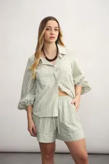 Camisa a rayas verticales color beige y blanco, con cuello clásico, cierre frontal con botón dorado, mangas largas abullonadas con puños elásticos, dos bolsillos frontales y corte holgado.