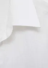 Camisa blanca de lino con cierre de botones frontal, cuello camisero, mangas largas con puños abotonados y corte recto.