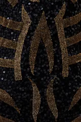 Vestido corto negro con lentejuelas doradas formando un patrón geométrico. Tiene breteles finos y escote recto.