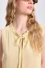 Vestido corto amarillo sin mangas, confeccionado en lino, con cuello con lazo y volados en el ruedo.