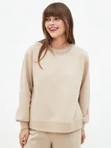 Buzo color beige con cuello redondo y detalle de apliques brillantes en el cuello.