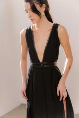 Vestido largo negro con escote en V profundo y detalles de ecocuero. Presenta un cinturón doble de ecocuero en la cintura y una falda amplia con dos aberturas laterales.