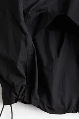 Campera negra de nylon repelente al agua y rompevientos con cuello elevado, cierre con protección para el mentón y bolsillos laterales con cierre. Modelo con hombros caídos, orificios de ventilación en las sisas y mangas murciélago con puños elásticos. Panel de ventilación en malla en la parte baja de la espalda y cordón para ajustar elástico con topes en el bajo. Forro de malla.
