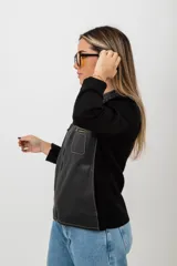 Campera negra con cuerpo de cuero y mangas de tejido de punto. Tiene cuello redondo, cierre frontal con cremallera, dos bolsillos con cremallera en el pecho y costuras decorativas en los hombros.