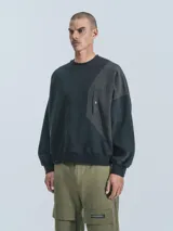 Buzo negro de cuello redondo, corte oversize y largo crop. Confeccionado en frisa gamuzada de algodón con recortes de microfibra y bolsillo delantero con cierre a presión.